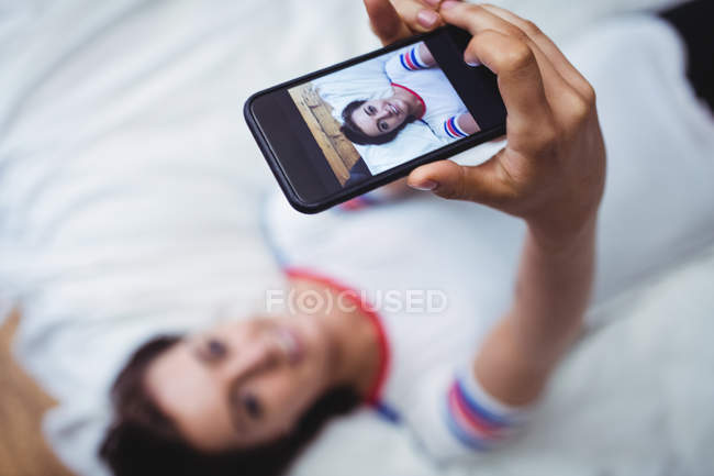 Женщина фотографирует себя на мобильный телефон в спальне — стоковое фото
