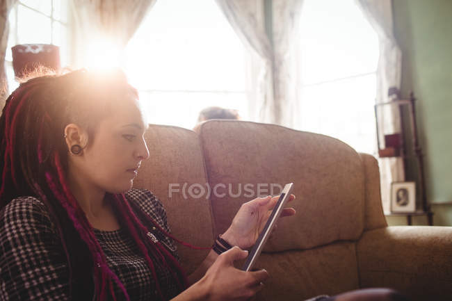 Молода хіпстерка використовує цифровий планшет, сидячи на дивані вдома — стокове фото