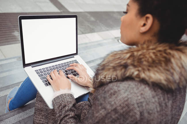 Frau tippt auf Laptop, während sie auf Stufen sitzt — Stockfoto