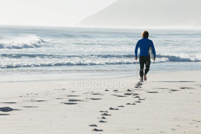 Surfista caminando en la playa en un día soleado - foto de stock