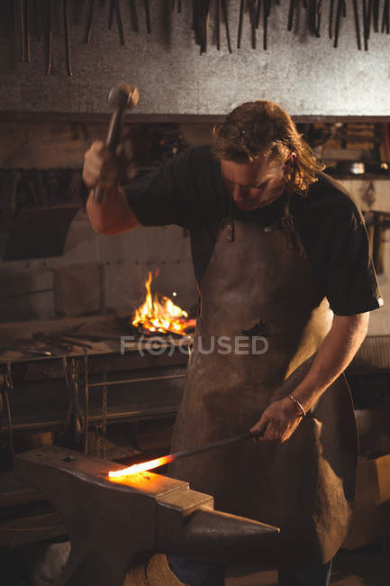 Ferreiro trabalhando em metal quente usando martelo para moldar na oficina — Fotografia de Stock