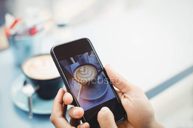 Mãos segurando telefone celular com fotografia de café no restaurante — Fotografia de Stock