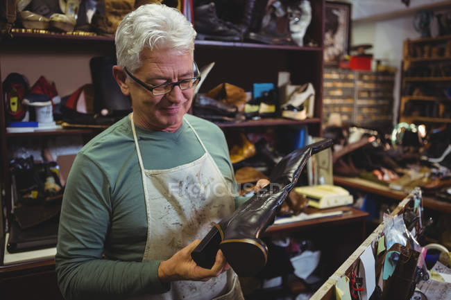 Zapatero maduro examinando un zapato en el taller - foto de stock