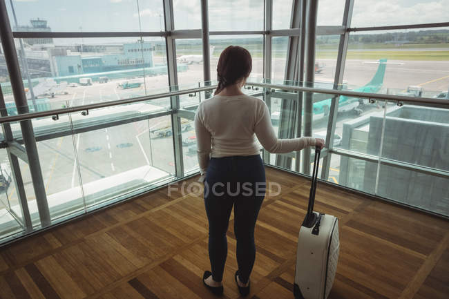Задній вид бізнес-леді з багажем дивлячись через скляне вікно в аеропорту — стокове фото
