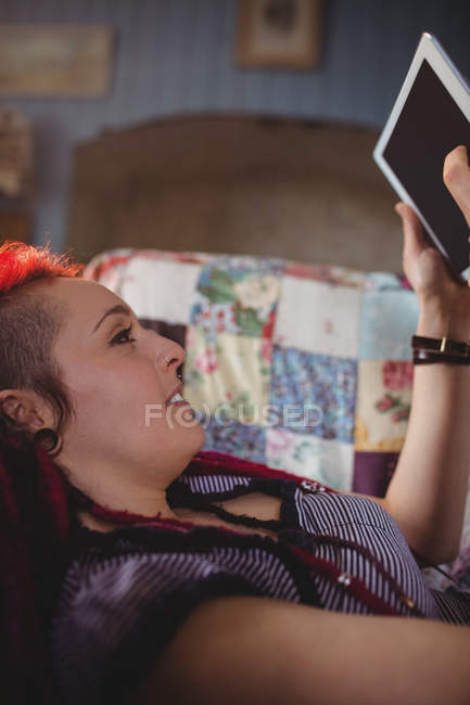 Hipster woman using digital tablet while relaxing on sofa at home — Stock Photo