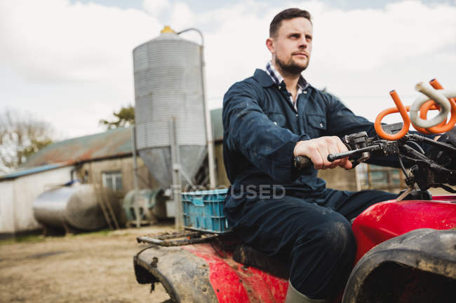 Smart farmer riding quadbike on field against silo — Stock Photo