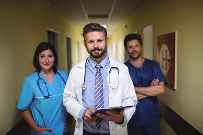 Team of doctors standing and looking in camera in hospital corridor — Stock Photo