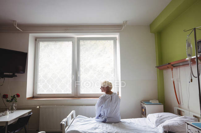 Старшая женщина, сидящая на кровати в больнице — стоковое фото