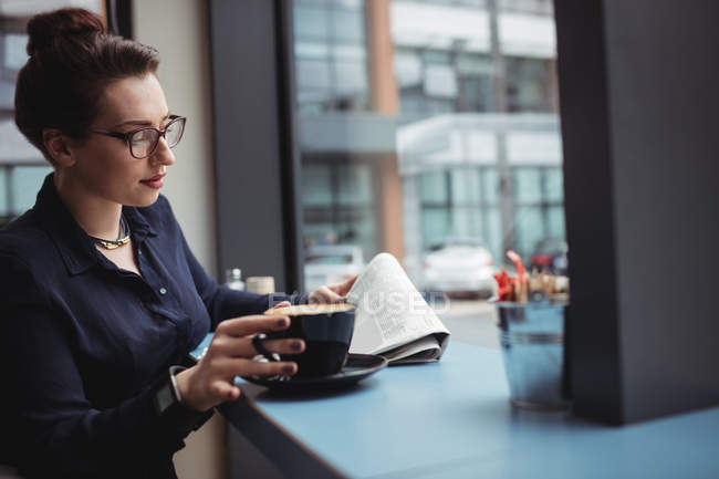 Young businesswoman reading newspaper in cafe — Stock Photo
