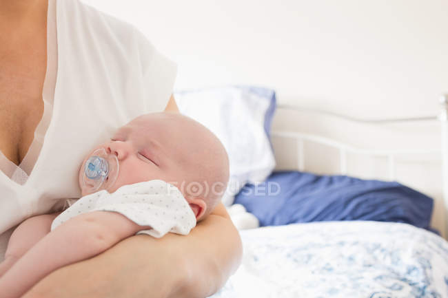Abgeschnittenes Bild eines Babys mit Dummy, der auf dem Arm der Mutter im Schlafzimmer schläft — Stockfoto