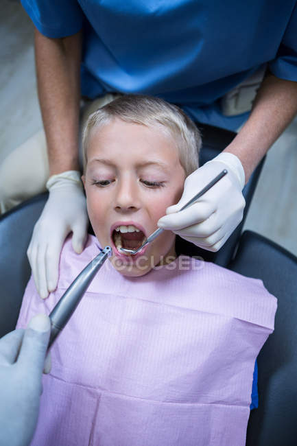 Dentista examinando um paciente jovem com ferramentas na clínica odontológica — Fotografia de Stock