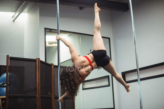 Vue arrière du danseur de pôle pratiquant la pole dance dans un studio de fitness — Photo de stock