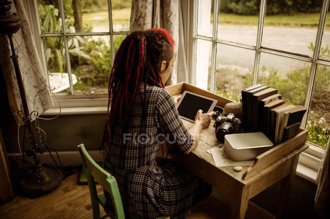 Вид ззаду жінки, використовуючи цифровий планшет за вікном вдома — стокове фото