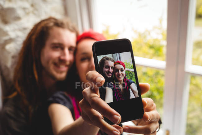 Feliz jovem casal tomando selfie pela janela em casa — Fotografia de Stock
