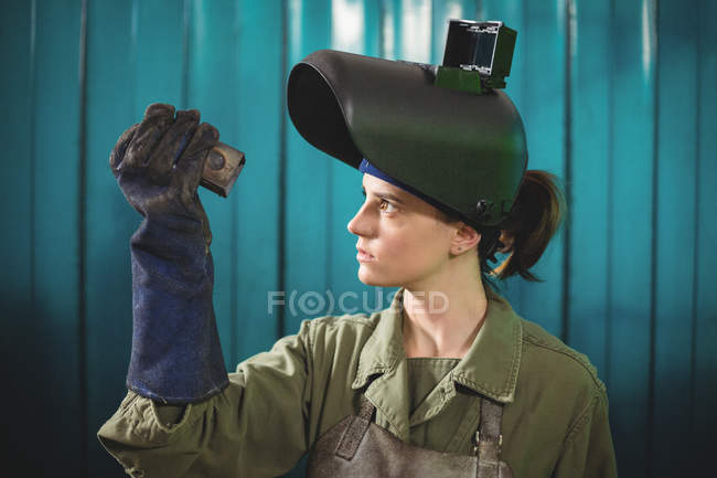 Soldador fêmea examinando peça de metal na oficina — Fotografia de Stock