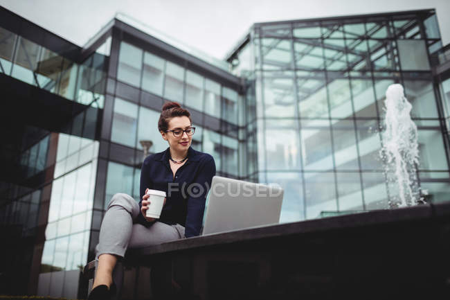 Jeune femme d'affaires utilisant un ordinateur portable contre un immeuble de bureaux — Photo de stock