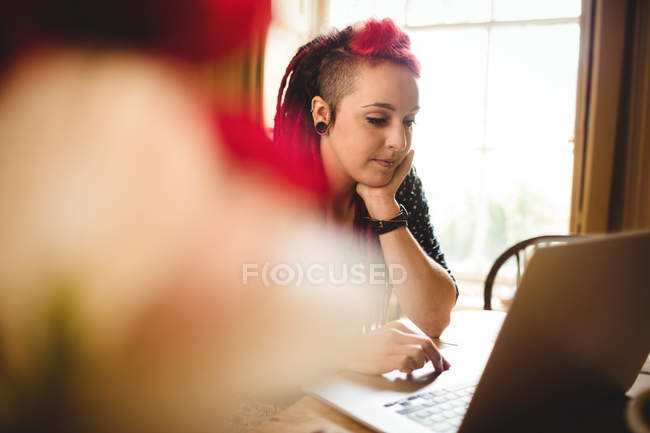 Mujer inteligente usando el ordenador portátil mientras está sentado en casa - foto de stock