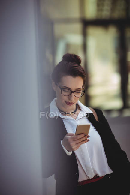 Молода бізнес-леді, використовуючи мобільний телефон, спираючись на стіну — стокове фото