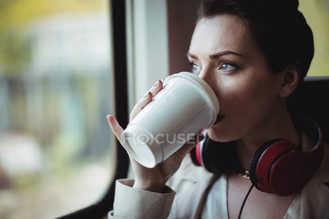 Pretty woman drinking coffee by window in train — Stock Photo