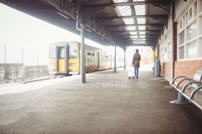 Vista trasera de la mujer que lleva equipaje mientras camina en la plataforma de la estación de tren - foto de stock