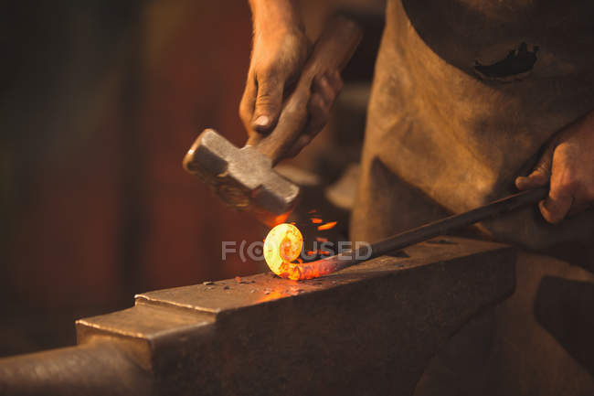 Ferreiro trabalhando em uma haste de ferro aquecido na oficina — Fotografia de Stock