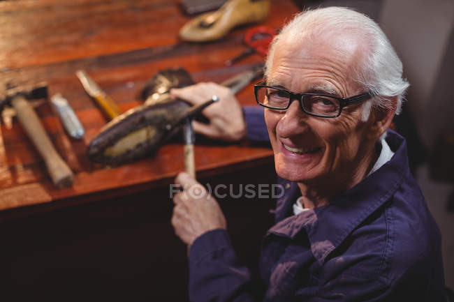 Sonriente zapatero senior golpeando un zapato en el taller - foto de stock