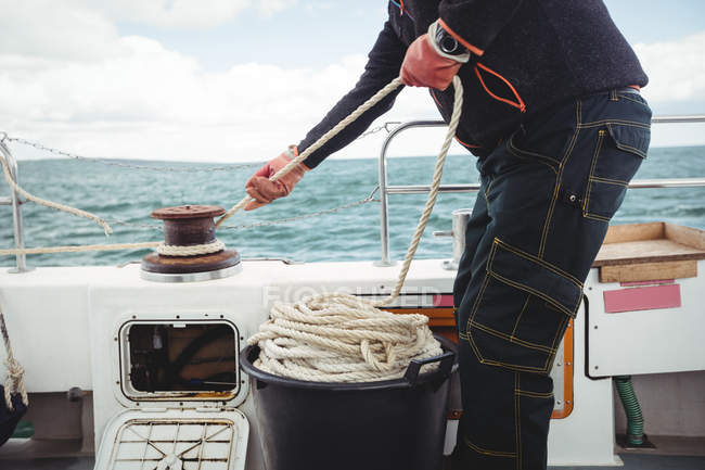Imagen recortada de pescador atando cuerda en pilona en barco - foto de stock
