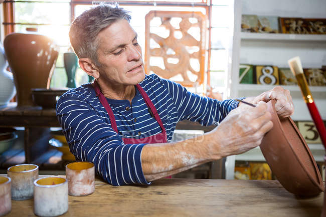 Male potter painting on pot in pottery workshop — Stock Photo