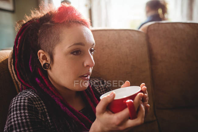 Frau trinkt Kaffee, während sie zu Hause auf dem Sofa sitzt — Stockfoto