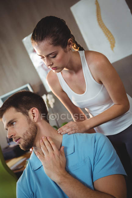 Physiothérapeute féminine examinant le cou d'un patient masculin en clinique — Photo de stock
