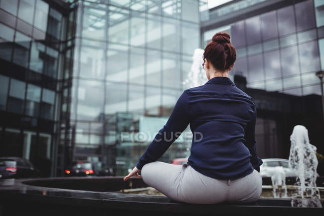 Vista trasera de mujer de negocios haciendo yoga contra edificio de oficinas - foto de stock