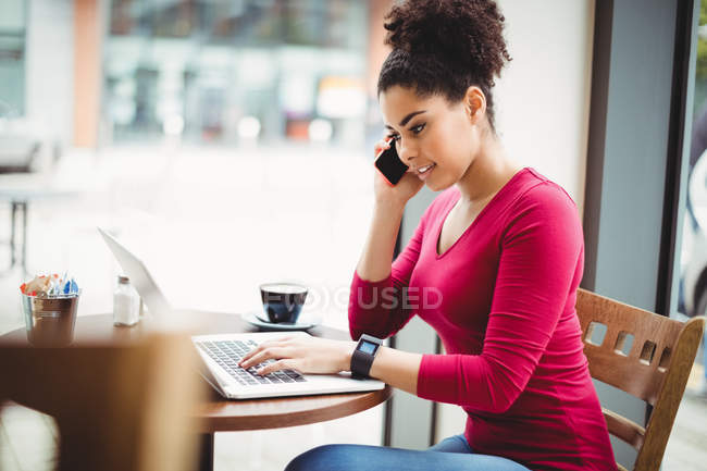 Young woman talking on mobile phone while sitting at restaurant — Stock Photo