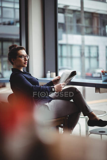 Geschäftsfrau hält Zeitung in der Hand, während sie im Café auf einem Stuhl sitzt — Stockfoto