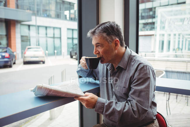 Man holding newspaper and having coffee in cafeteria — Stock Photo