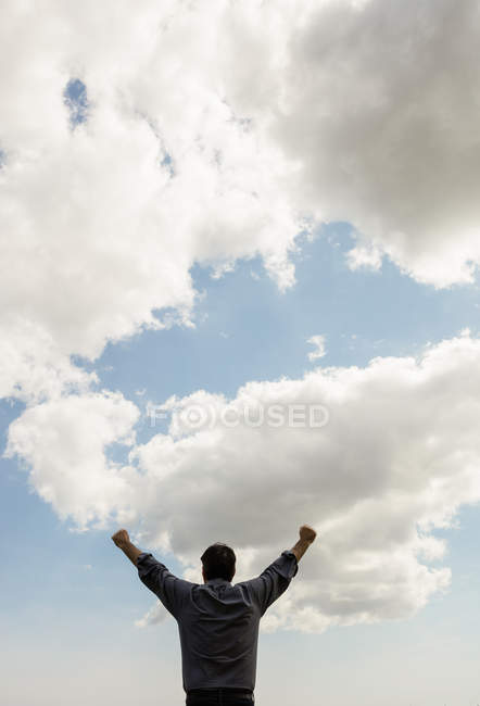 Vue à angle bas de l'homme avec les bras levés contre un ciel nuageux — Photo de stock