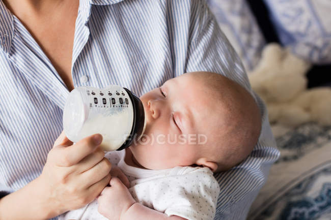 Imagem cortada de mãe alimentando bebê com mamadeira em casa — Fotografia de Stock