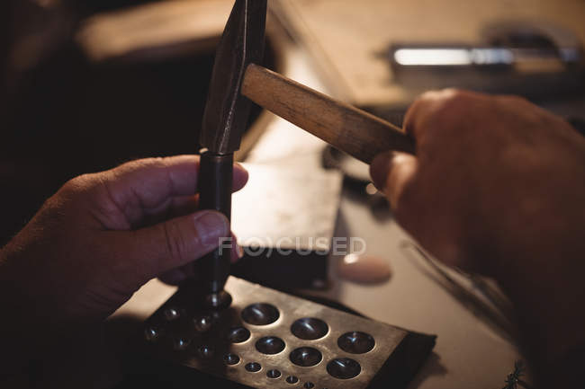 Cropped image of goldsmith making hole in sinking at workshop — Stock Photo