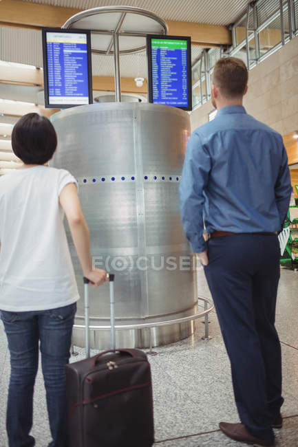 Travellers looking at departure and arrival screen board displays in airport — Stock Photo