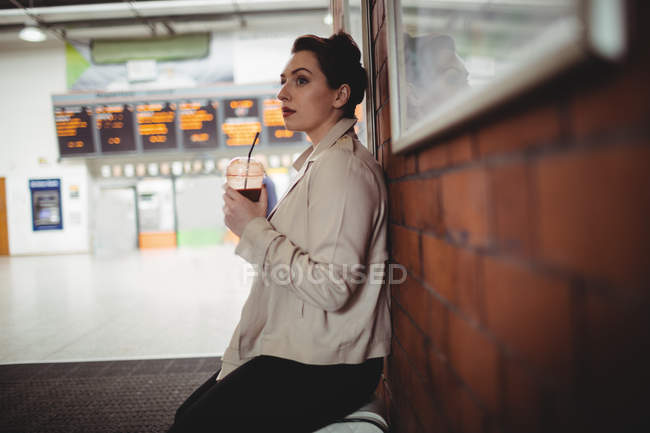 Jovem mulher cuidadosa segurando bebida na estação ferroviária — Fotografia de Stock