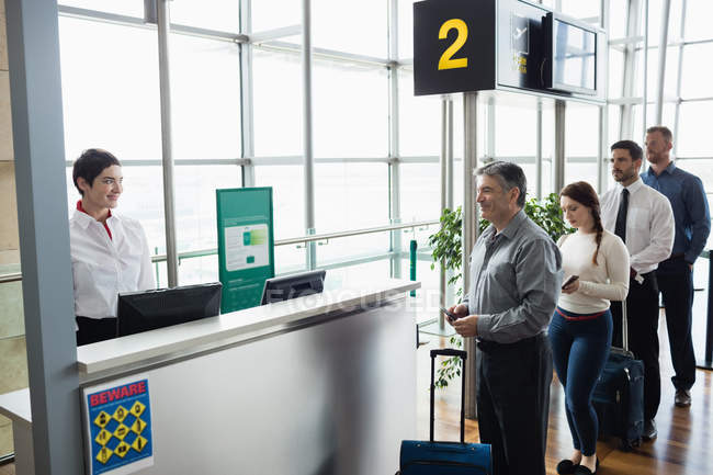 Pasajeros esperando en cola en el mostrador de facturación en la terminal del aeropuerto - foto de stock