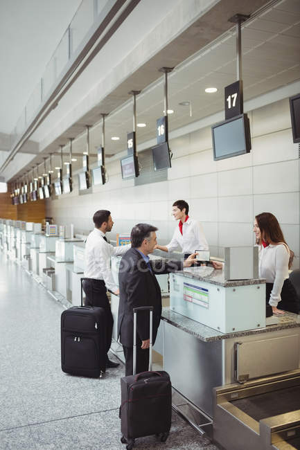 Asistentes de facturación de aerolíneas entregando pasaporte a los pasajeros en el mostrador de facturación del aeropuerto - foto de stock