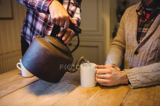 Средняя часть женщины наливает воду с чайником дома — стоковое фото