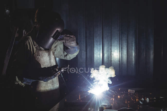 Soldador feminino trabalhando em peça de metal na oficina — Fotografia de Stock