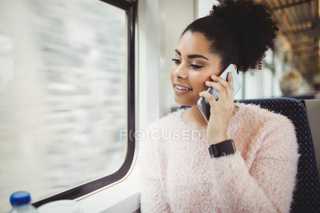 Усміхнена жінка розмовляє по телефону, сидячи в потязі — стокове фото