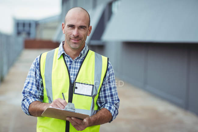 Portrait of construction worker writing on clipboard outside office — Stock Photo