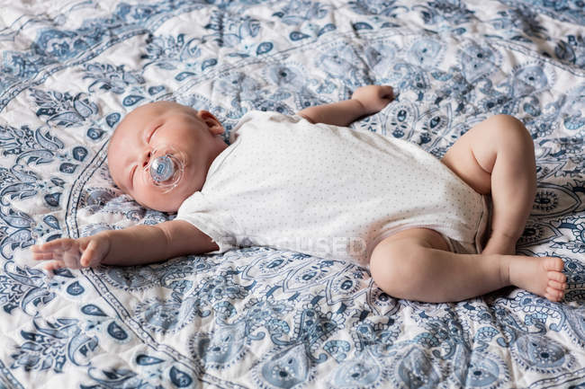 Bebê dormindo com manequim na boca na cama em casa — Fotografia de Stock