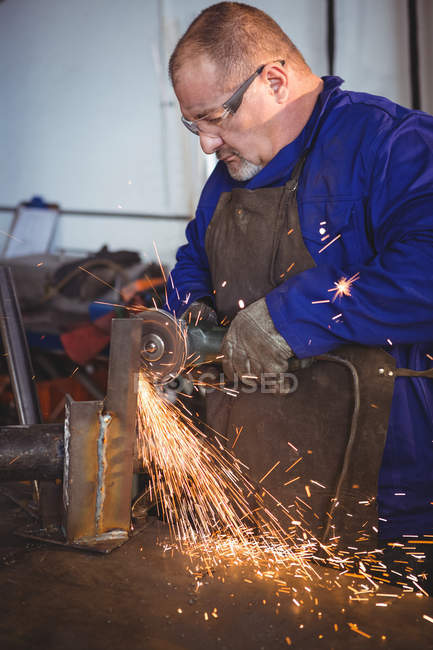 Welder sawing metal with electric tool in workshop — Stock Photo