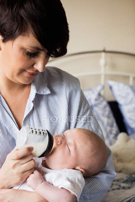 Close up of mother feeding baby with milk bottle at home — Stock Photo
