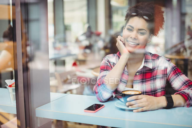 Портрет улыбающейся молодой женщины, увиденной через окно ресторана — стоковое фото