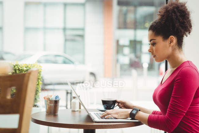 Mulher usando laptop enquanto sentado no restaurante — Fotografia de Stock